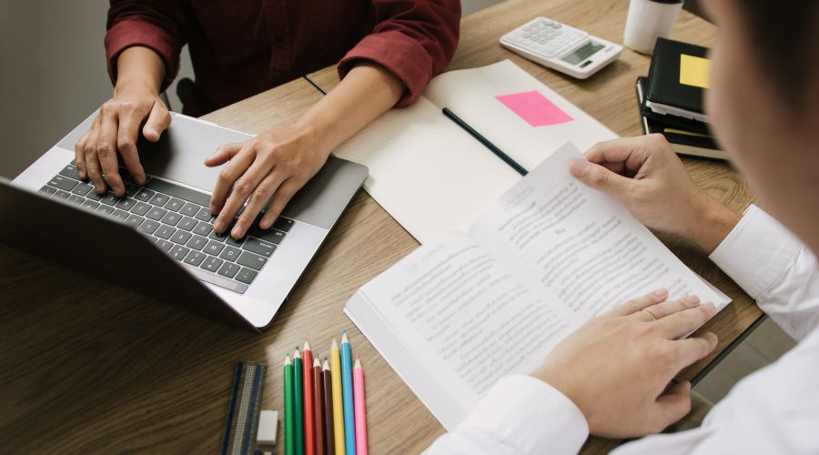 Deux paires de mains d'étudiants : l'une tape sur un clavier, l'autre lit un livre