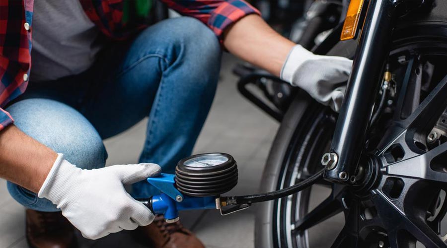 man checking the pressure of a motorbike tyre with a pressure gauge