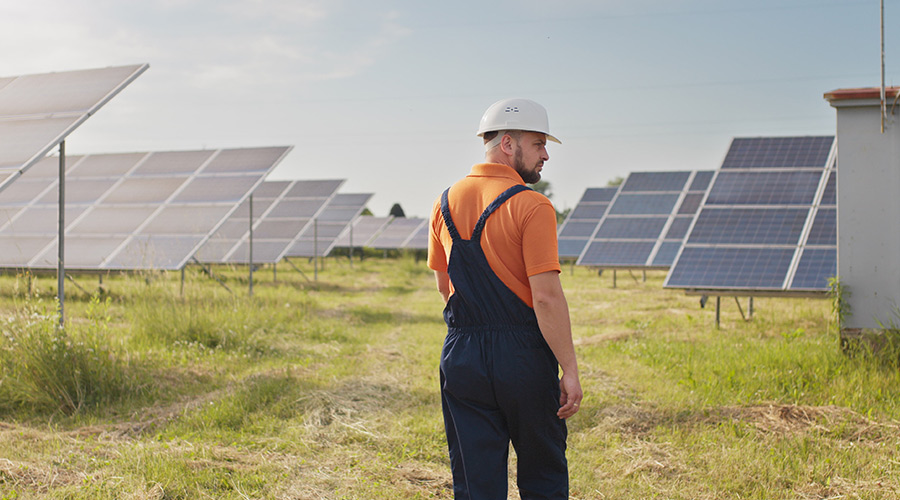 "Um homem com roupa de trabalho num campo com painéis solares".
