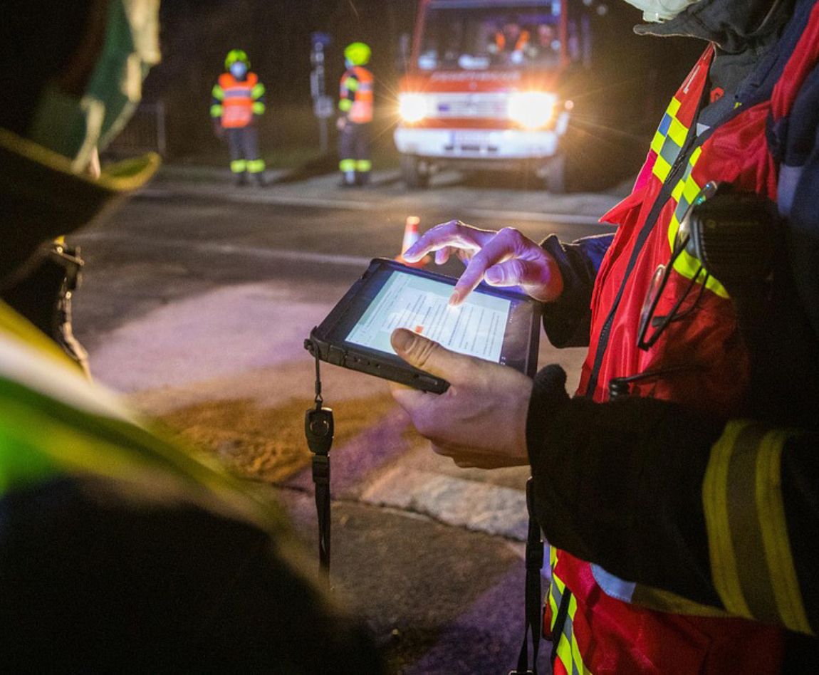 Pompiers en intervention de nuit utilisant une tablette pour la coordination des secours.